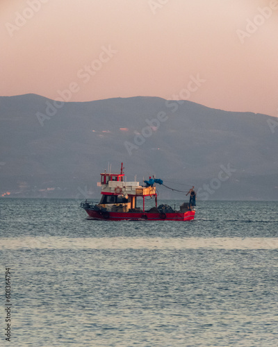 A red fairy boat in the middle of the ocean with mountains in the background at sunset
