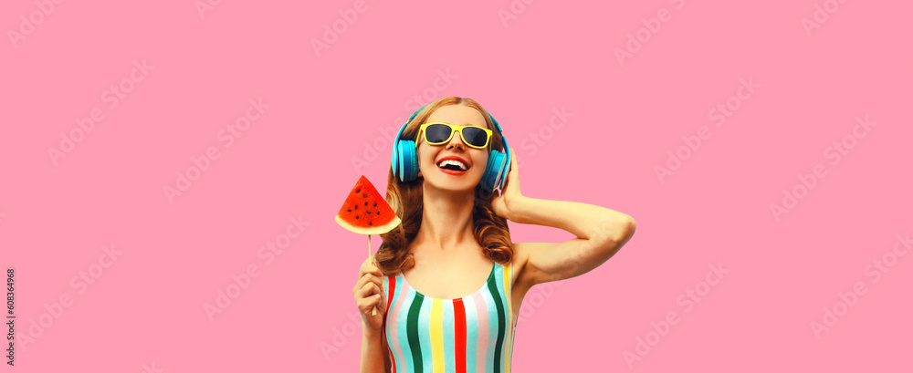 Summer colorful portrait of cheerful happy laughing young woman in headphones listening to music with juicy lollipop or ice cream shaped slice of watermelon on pink background
