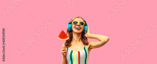 Summer colorful portrait of cheerful happy laughing young woman in headphones listening to music with juicy lollipop or ice cream shaped slice of watermelon on pink background © rohappy