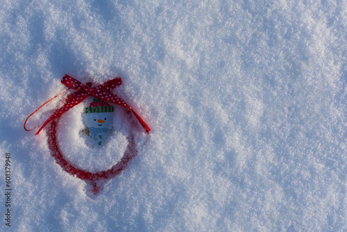 Christmas wooden toy snowman with red bow and ball, lying on a snowy background in winter. Copy space. Greeting card.