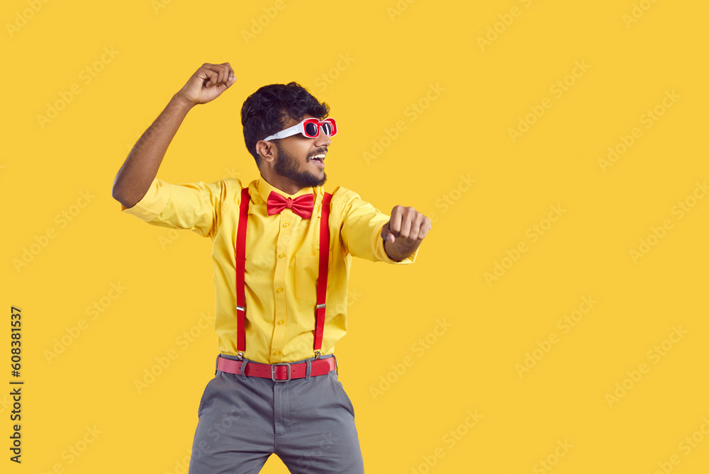 Happy man dancing and having fun. Portrait of funny young Indian guy wearing yellow shirt, red suspenders, bow tie and sunglasses dancing gangnam style isolated on color background. Party concept - obrazy, fototapety, plakaty 