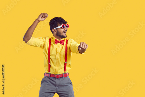 Happy man dancing and having fun. Portrait of funny young Indian guy wearing yellow shirt, red suspenders, bow tie and sunglasses dancing gangnam style isolated on color background. Party concept