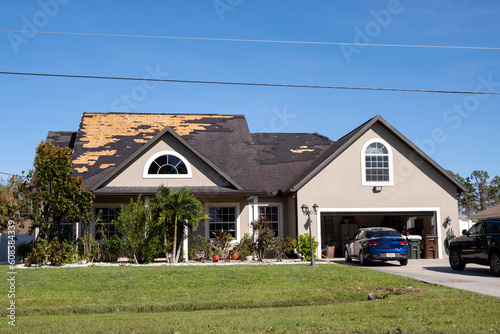 Damaged house roof with missing shingles after hurricane Ian in Florida. Consequences of natural disaster