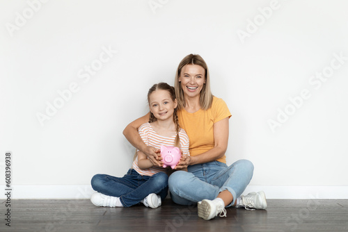 Family Budget. Smiling Beautiful Mother And Little Daughter Holding Piggy Bank