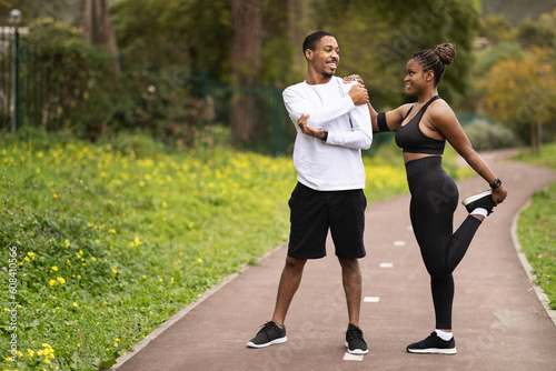 Positive young black couple with phone doing leg exercises, warm-up before running, enjoy sports