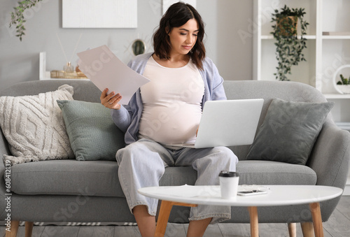 Young pregnant woman working with documents and laptop at home © Pixel-Shot