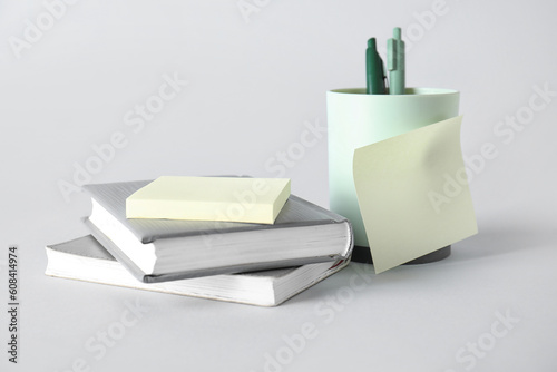 Pen holder with sticky notes and books on grey background photo