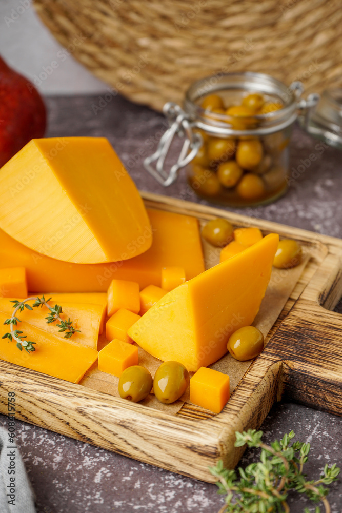 Board with tasty cheddar cheese, olives and thyme on grunge background, closeup Board with tasty cheddar cheese, olives and thyme on grunge background, closeup