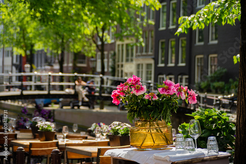 Charming restaurant table with glasses and flowers near the canal, streets of Amsterdam,