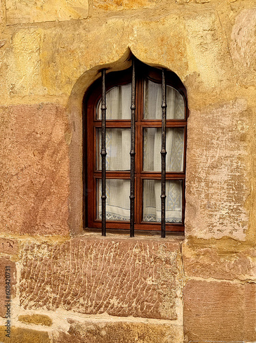A beautiful antique window made of modern materials in a stone wall of an old restored house protected by figured decorativel bars