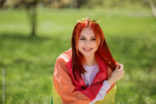 Posing in front of the camera very charismatic beautiful red hair lady posing in front of the camera she wearing sunglasses and feeling nice holding the lgbt flag