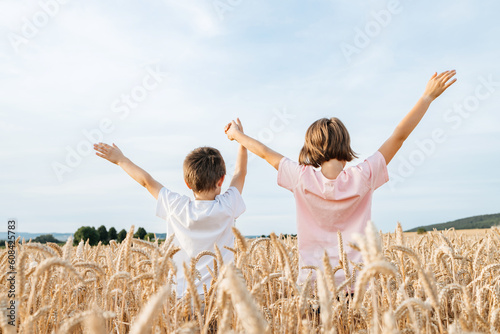 Happy boy and girl stand in a field with ears of rye and hold hands. Happy and free children in the summer on vacation. Vacation concept.