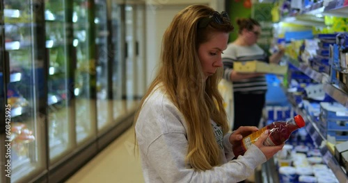 Young woman in grocery store or supermarket read label on drink plastic bottle. Mother study composition and ingredients of food product to make healthy and conscious choice.