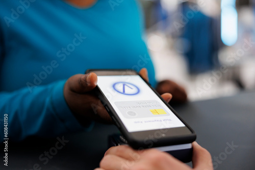 African american woman paying for formal wear with mobile phone nfc on pos terminal, buying stylish clothes and accessories in modern boutique. Shopper standing at retail store counter desk. Close up