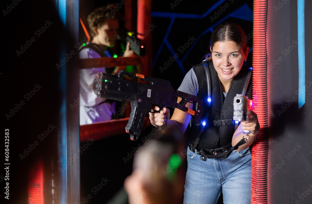 Smiling girl with laser pistol during playing laser tag with her friends in dark room