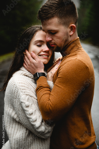 beautiful couple in winter sweaters hugging being on a mountain road overlooking the forest