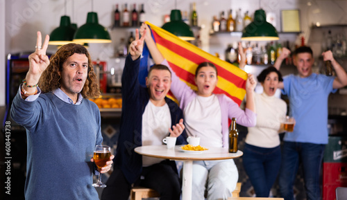 Excited sports supporters of different ages with flag of Estelada, rejoicing winning game with beer and snacks in pub photo