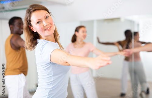 Group of positive smiling young adult people dancing in pairs during lesson in dance class, indoors