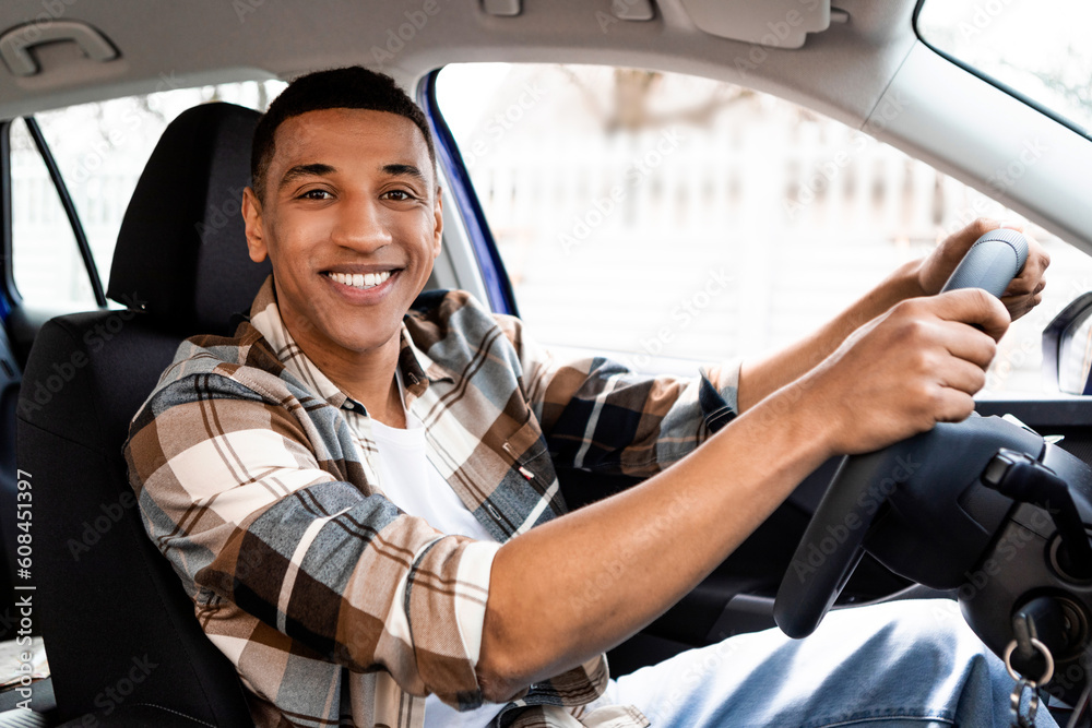 Portrait of happy young african american man driving car, looking and smiling at camera, enjoying road trip. Automobile ownership concept