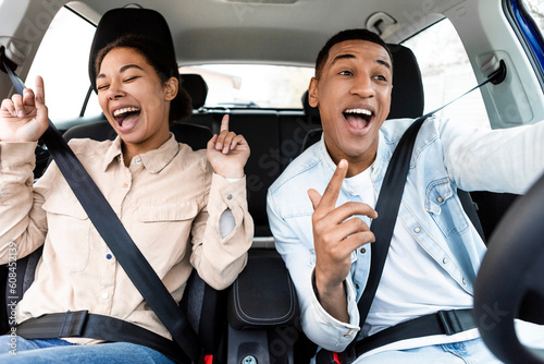 Joyful black lady and man singing, dancing and enjoying travel in car together, being in good mood, buying new car, weekend trip and road at journey