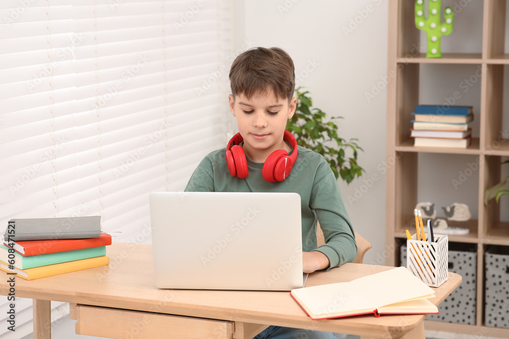 Boy with red headphones using laptop at desk in room. Home workplace Boy with red headphones using laptop at desk in room. Home workplace