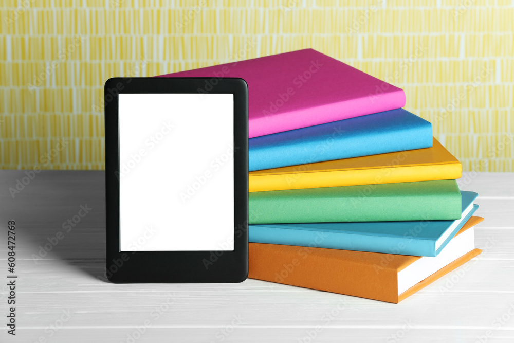Portable e-book reader and stack of books on white wooden table Portable e-book reader and stack of books on white wooden table