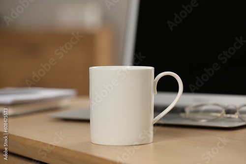 White ceramic mug and laptop on wooden table at workplace