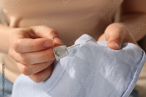 Bilde på lerret Woman sewing on light blue fabric with thimble and needle, closeup