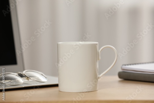 White ceramic mug, glasses and laptop on wooden table at workplace