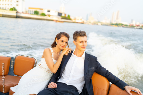 Caucasian couple enjoy urban outdoor lifestyle travel city on luxury private boat yacht sailing in the river with celebrating holiday event drinking champagne together on summer vacation at sunset.