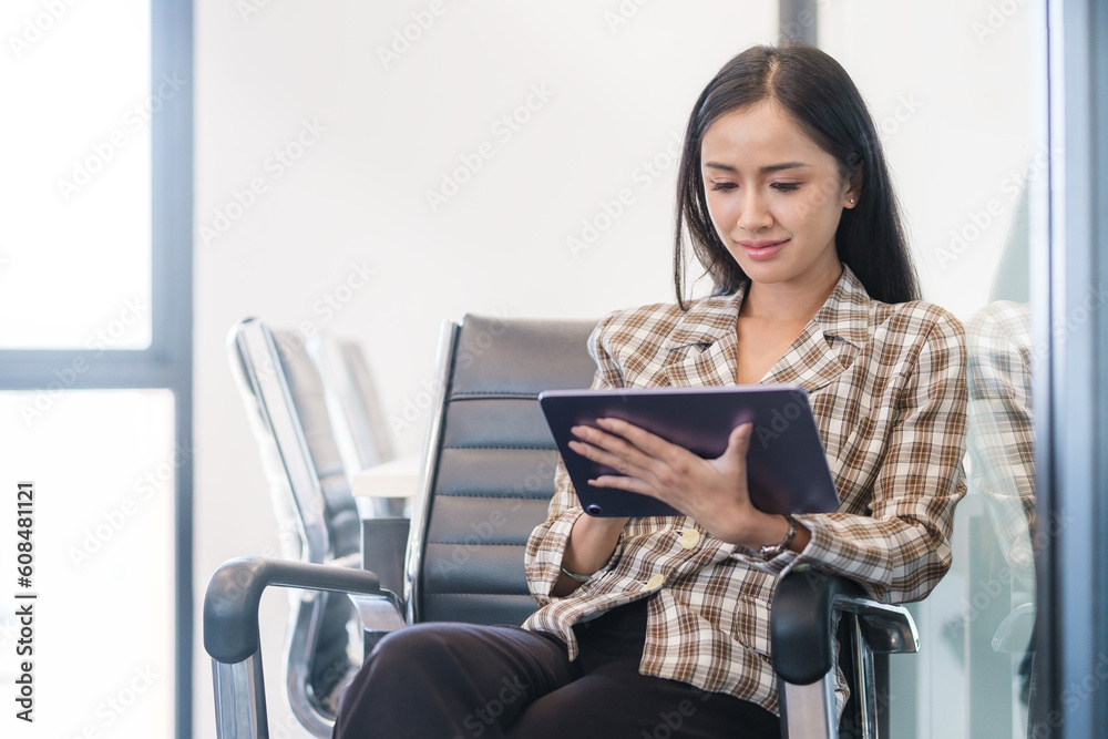 Attractive female manager sitting on office chair in meeting room and using digital tablet. Attractive female manager sitting on office chair in meeting room and using digital tablet.