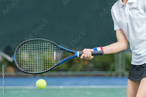 Shot of sportswoman hitting tennis ball with racket while training on court in sunny summer day. © wattana