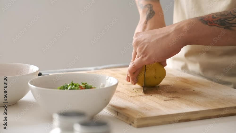 Young unrecognizable tattooed latin man cutting a lemon and adding the juice to the pico de gallo.