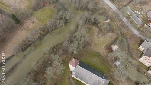 Aerial birdseye view of high water in springtime, flood, Durbe river (Latvia), Cirava city, brown and muddy water, sunny day, wide drone shot moving forward over the rooftops photo