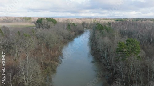 Aerial establishing view of high water in springtime, Barta river (Latvia) flood, brown and muddy water, sunny day, wide ascending drone shot moving forward photo