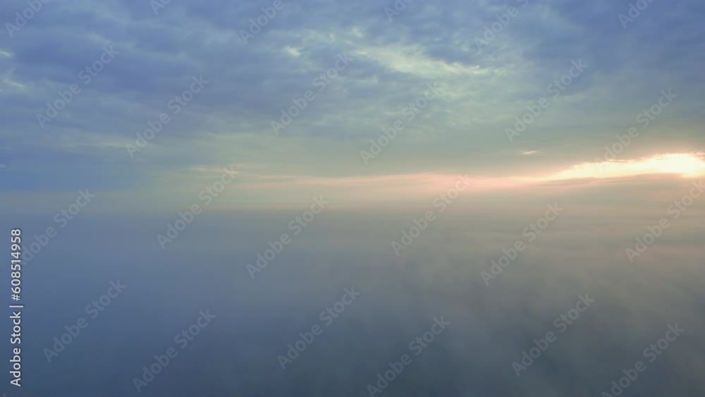 Sunrise in the fog from a drone in Africa. The low down clouds light up from the rising sun, with blue and gold colours. Humid landscape after the rain season