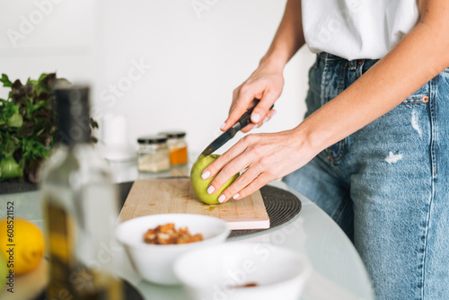 Young slim woman in white t-shirt and blue jeans cooking healthy food with apple in kitchen at home