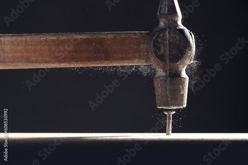 An old hammer hits a nail close-up on dark background. Dust rises from the impact. Carpentry concept.