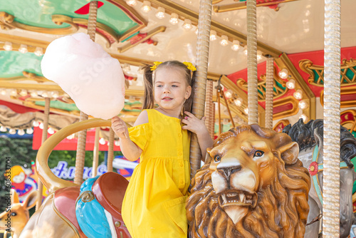 Adorable little girl in summer yellow dress at amusement park having a ride on the merry-go-round