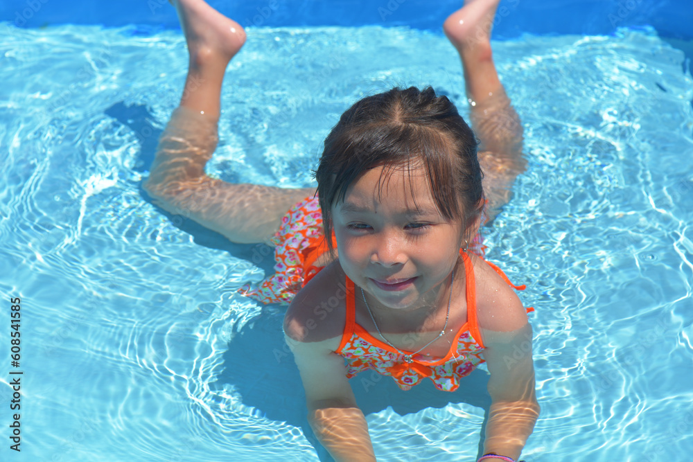 Happy little girl swimming pool on a hot summer day. Kids learn to swim. Child water toys. Children play in tropical resorts. Family beach vacation.