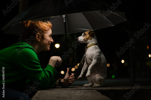 Red-haired woman and dog jack russell terrier under an umbrella in the dark. 