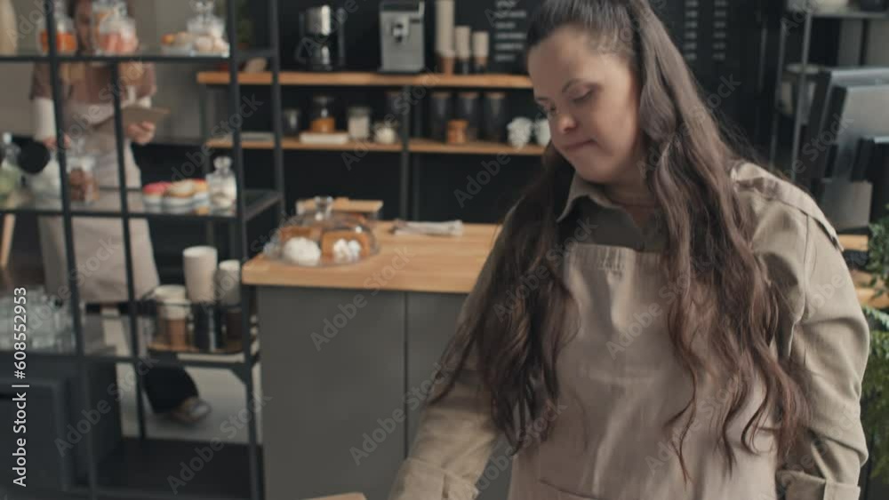 Young waitress with disability giving terminal to unrecognizable female customer to pay for lunch in cafe, woman paying for it using smartphone