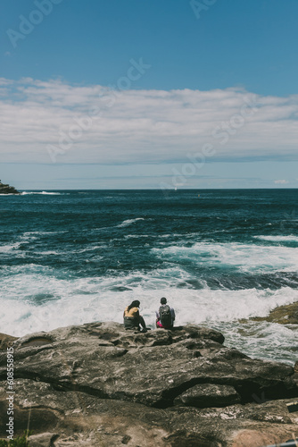 Wide shot of a couple sitting on rocks and enjoying the ocean view