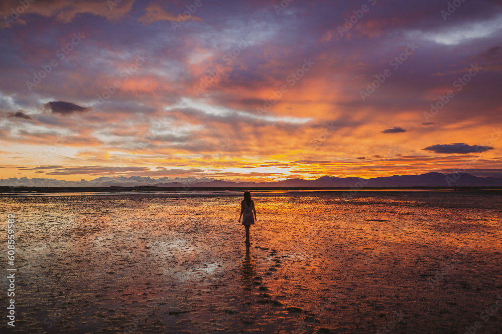 Vertical shot of a female model walking on a beach in front of a mesmerizing view of the sky and clouds