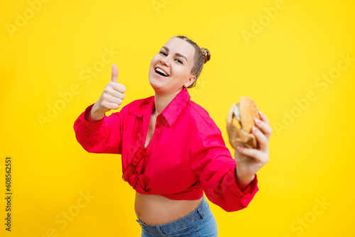 Close-up of a pregnant woman in a bright pink shirt and junk food. Hamburger and pregnancy. The concept of a pregnant woman eating unhealthy food. Cheerful pregnant woman eats fast food © Дмитрий Ткачук