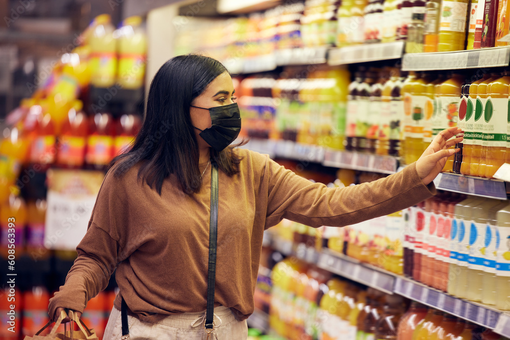 Grocery shopping, woman and juice at a shop, market and store for groceries sale with mask. Health, virus safety and female person with orange and healthy drink purchase in a supermarket at shelf