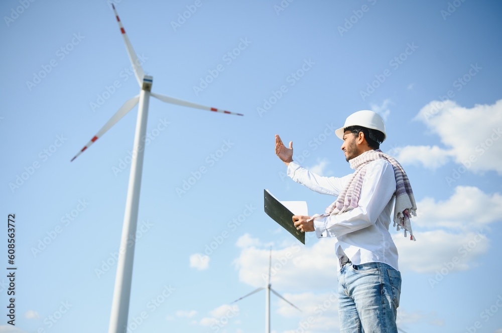 Portrait of focused indian man standing on field with wind turbines Portrait of focused indian man standing on field with wind turbines