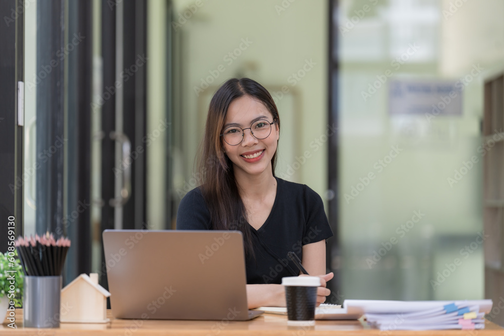 Portrait of a young beautiful Asian woman smiling and looking at the camera while sitting at her office desk. Portrait of a young beautiful Asian woman smiling and looking at the camera while sitting at her office desk.