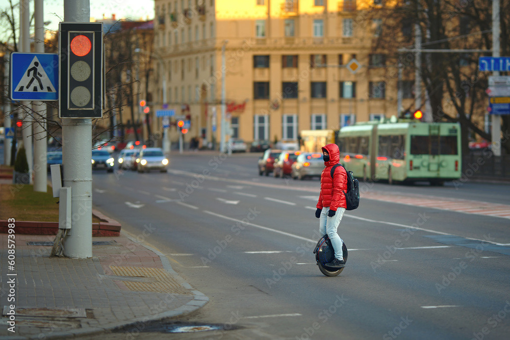 Unrecognizable man cross road on electric unicycle, commuting to work. Portable individual transportation vehicle. Man on electric monowheel (EUC). Stylish guy moves along sidewalk on mono wheel