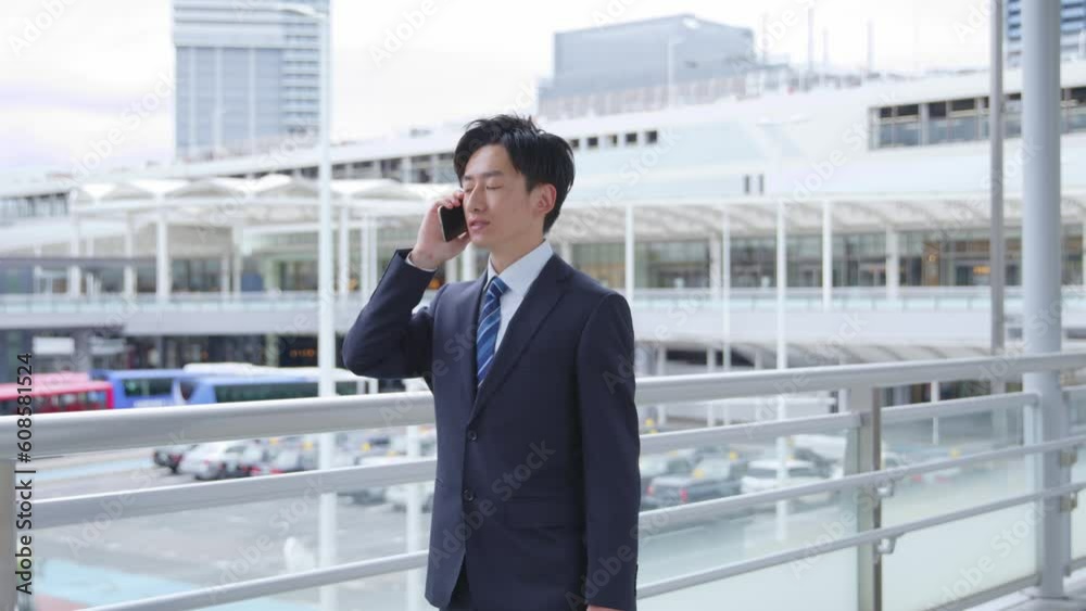 駅にてスマートフォンを使用して仕事をするスーツを着た若い日本人ビジネスマン 駅にてスマートフォンを使用して仕事をするスーツを着た若い日本人ビジネスマン